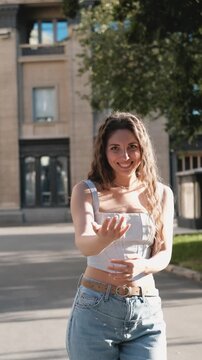 A portrait of a cheerful girl with long curly hair smiling at the camera. A close-up portrait of a friendly young woman in casual clothes against a blurred city background. Outdoors.