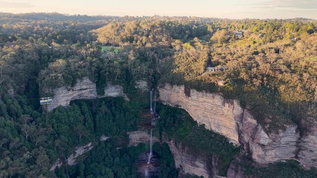 Aerial drone shot from a different angle of Katoomba Falls, showing the waterfall, surrounding forest and cliffs from a wider perspective in the Blue Mountains.
