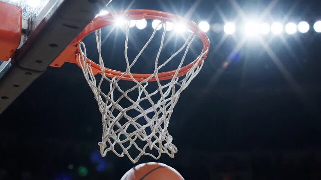 Basketball Going Through Hoop With Bright Stadium Lights in Background During Night Game Close Up