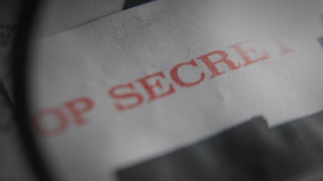 Magnifying glass pointing on red stamp of Top Secret security clearance on classified intelligence report or military government document file. Leaked papers by whistleblower or exposed confidential