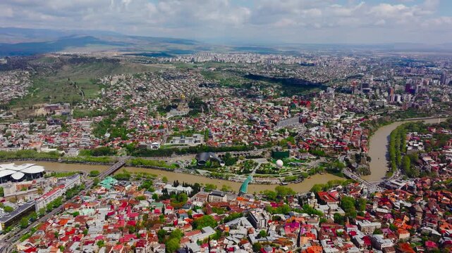 Aerial drone view of Tbilisi, Georgia showcasing a dynamic cityscape with river, bridges, historic districts and modern skyline.