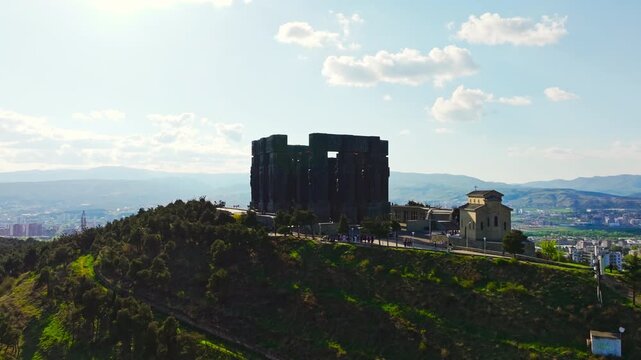 High aerial drone shot of the Chronicles of Georgia monument revealing monumental stone pillars and sweeping views of Tbilisi surroundings.