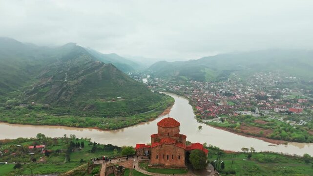 Breathtaking cinematic drone sweep over a historic Georgian monastery perched above a winding mountain river. Golden hour light illuminating the rugged Caucasus landscape. 4K stock video.