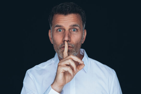 Portrait of man with finger on his mouth in front of black background