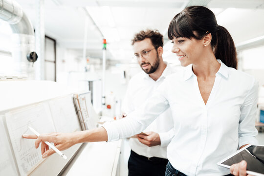 Smiling female technician pointing at graph while discussing with male colleague at laboratory