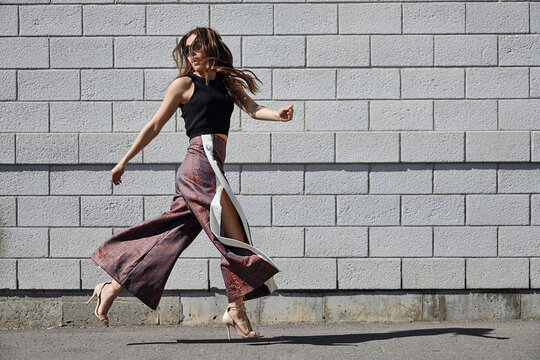 Fashionable young woman passing brick wall