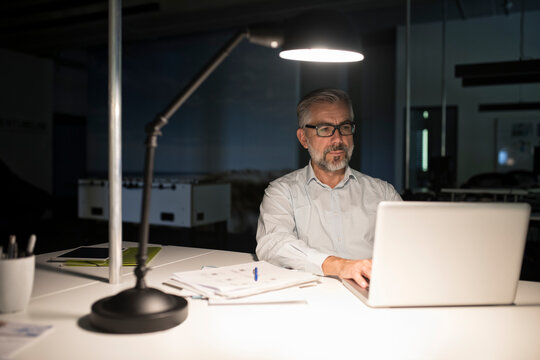 Businessman in office using laptop in the dark