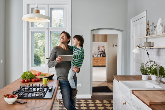 Father and son using tablet in kitchen looking at ceiling lamp