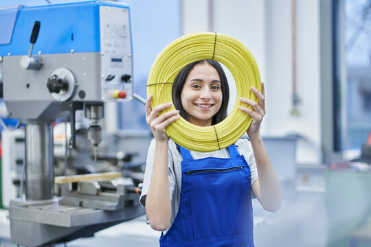 Happy female worker looking through rolled up cables in factory