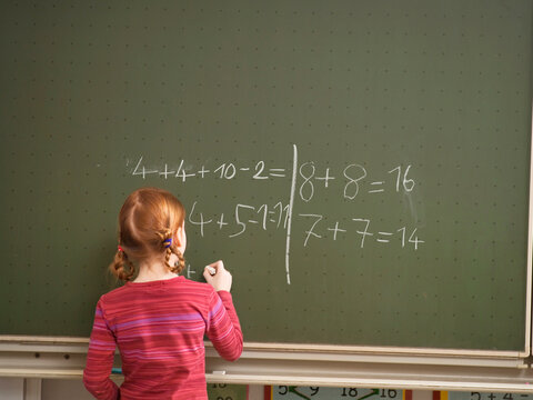 Girl (4-7) writing on blackboard, rear view