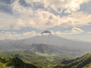Fototapeta premium Volcanic Mountain Over Green Valley Under Cloudy Sky