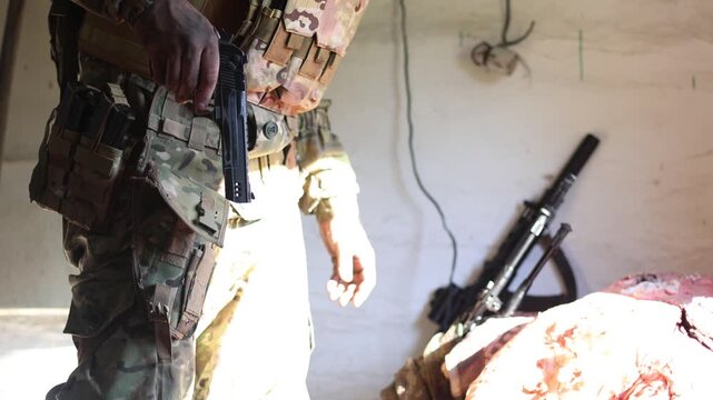 A soldier in camouflage combat gear draws a pistol from its holster and cocks it. A close-up of his hands and the holster. Slow motion 4K footage.
