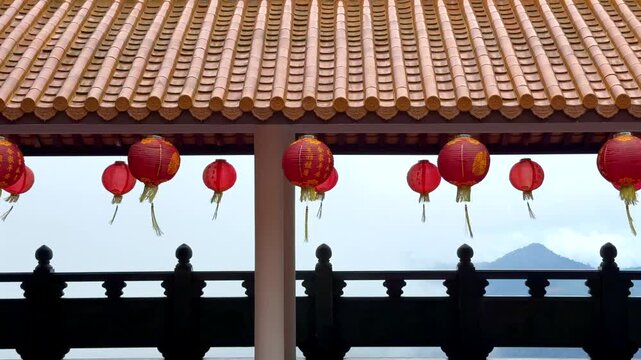 Red Chinese Lanterns with Misty Mountain View. Traditional red Chinese lanterns hanging under a tiled roof with foggy mountains in the background. Peaceful temple travel view.