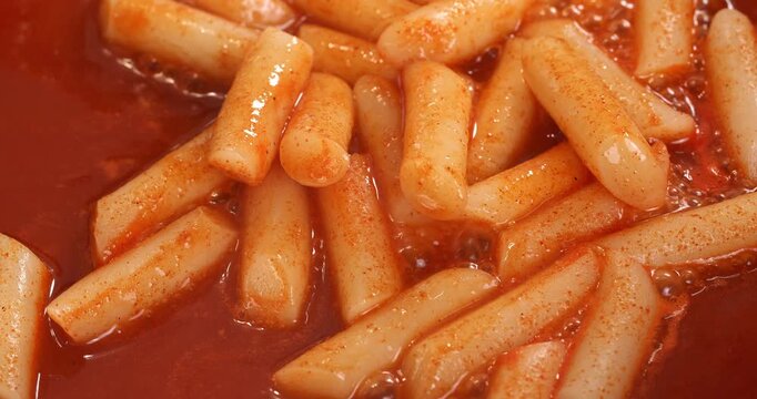 Process of cooking the Korean national dish tteokbokki. The tteokbokki in sauce are fried in a pan and stirred with chopsticks.