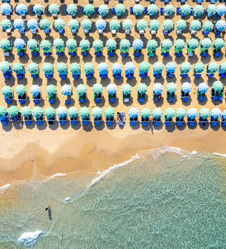 Aerial view of Bat Yam beach featuring rows of turquoise and blue umbrellas on golden sand by clear Mediterranean water in Bat Yam, Center District, Israel.