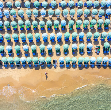 Aerial view of Bat Yam beach with rows of turquoise umbrellas and sunbeds on golden sand by the clear Mediterranean sea, Bat Yam, Center District, Israel.