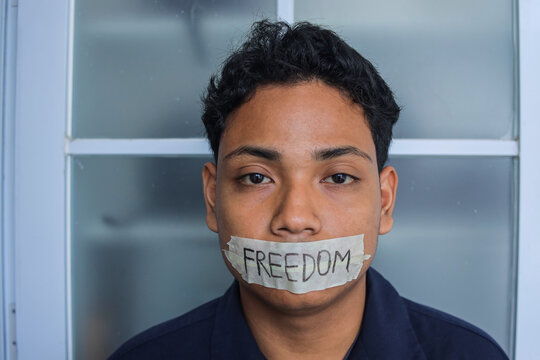 Young Man Looking At Camera With Masking Tape Over His Mouth That Says Freedom