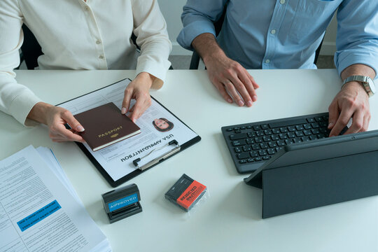 Close up of middle aged colleagues reviewing visa application, holding passport and processing approval at desk. Suitable for immigration services, travel documentation marketing