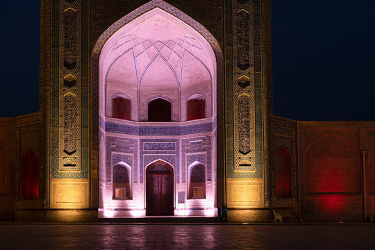 Kalyan Madrasah illuminated at night in Bukhara with colorful tile work and pointed arch portal. Ideal for travel, tourism, and cultural heritage publications.