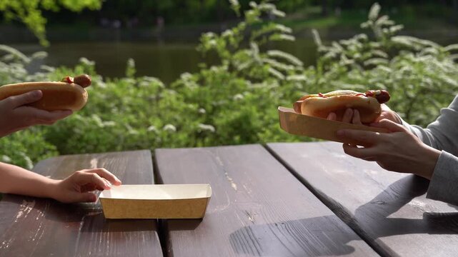 Cinematic video of hands taking hot dogs from a wooden table at an outdoor summer cafe. Casual street food lifestyle moment with natural light