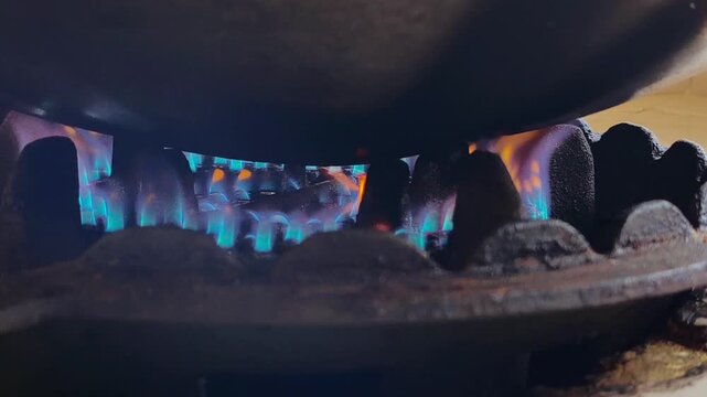 blue gas flame ignited on an old rusty kitchen stove during home cooking, symbol of daily energy use and rising fuel price