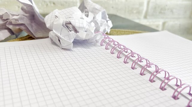 Writer's block concept with crumpled paper balls thrown on an empty spiral notebook page, symbolizing the frustration and challenge of the creative search for new ideas