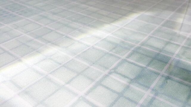 Pleated window blind moving in the sunlight, creating an abstract background of light and shadow, highlighting the fabric's square texture and geometric pattern