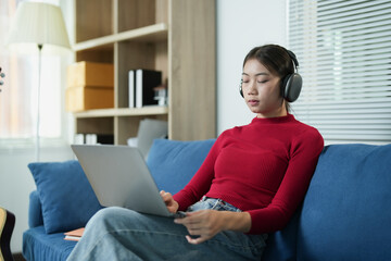 Obraz premium Young woman relaxing on sofa at home, wearing headphones, studying, concentrating, listening to music or an online lecture while working on a laptop computer