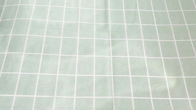 Green fabric with a white grid pattern being folded, revealing a smooth and textured background perfect for minimalistic and contemporary design projects