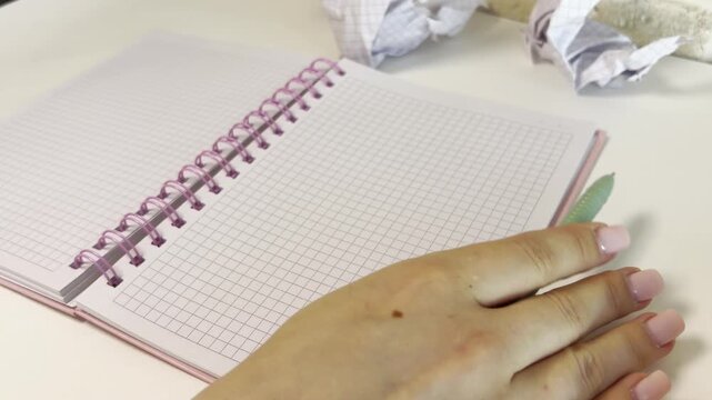 Frustrated woman with writer's block crumpling paper and turning blank pages of a notebook, a creative crisis concept of starting over on a clean slate