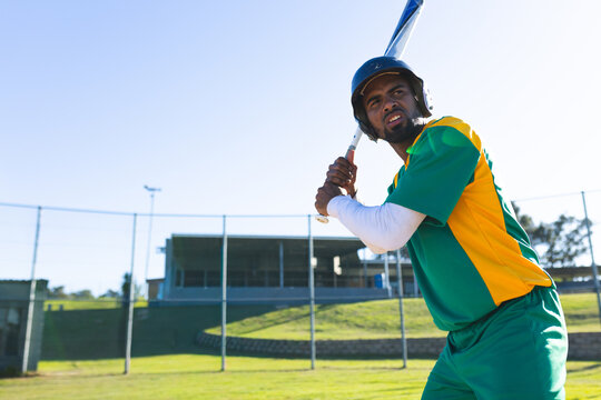 Asian man batting on baseball field wearing team uniform with helmet holding bat, copy space