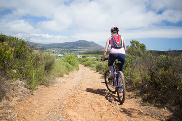 Fototapeta premium Female in twenties riding mountain bike on rocky trail with helmet and red pack, copy space