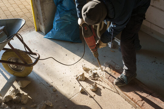 Worker using jackhammer to break concrete floor during renovation