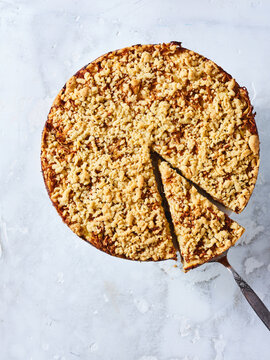 A freshly baked apple pie with a crumbly topping and a slice being served. Ideal for use in dessert menus, online bakery promotions, recipe blogs, and packaging for homemade products
