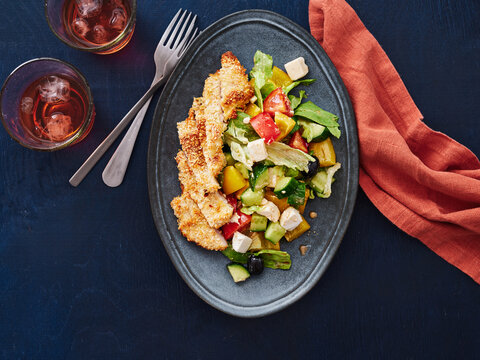 This composition features a crispy chicken salad served on a dark plate alongside two glasses of iced beverage. Ideal for restaurant menus, food blogs, and advertising healthy dining options