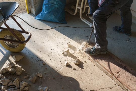 Worker using jackhammer to break concrete floor during renovation