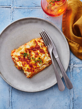 This photo features a slice of lasagna topped with cheese and herbs, served with cutlery on a plate