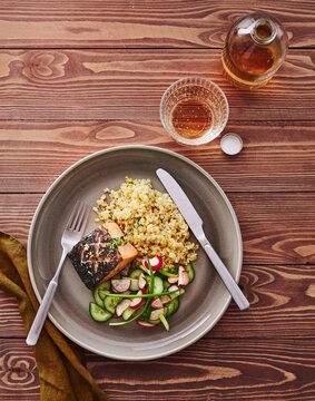 The plate features grilled salmon served with quinoa and a fresh cucumber salad accompanied by a drink. This image is suitable for menu design, food blogs, and advertising for healthy meal options