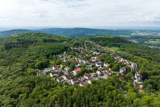 Drone aerial view of Kelkheim-Eppenhain in Hesse, Germany, surrounded by dense forests and rolling hills of the Taunus mountain range under dramatic cloudy skies