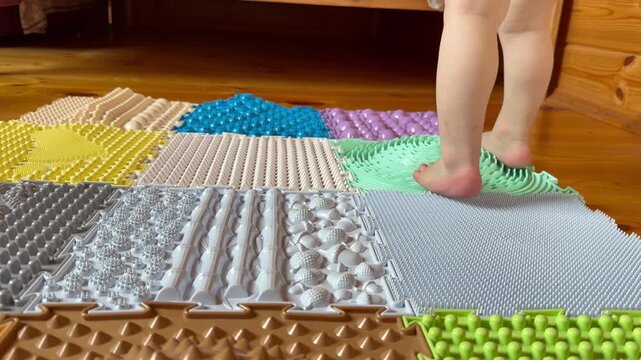 A close-up shot of a child's bare feet walking on various textured orthopedic puzzle mats. 