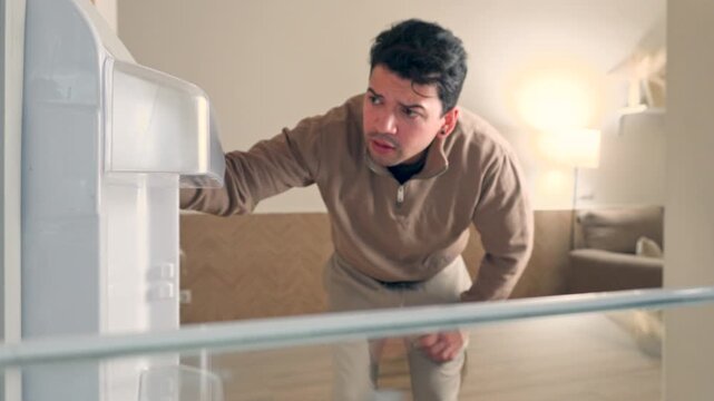 man opening empty fridge looking inside disappointed and taking a single brown egg in a cinematic horizontal view shot of hungry person in the kitchen