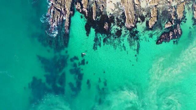Drone aerial landscape showing a lone kayaker cruising on water above clear ocean reef along sandbar beside rocky terrain headland at Mossy Point Tomakin Beach South Coast Australia leisure fitness