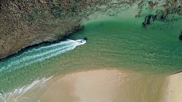 Drone aerial landscape of a fishing boat cruising through Tomaga River channel surrounded by rocky headland reef and sandy shoreline at Mossy Point Tomakin on the South Coast Australia marine tourism