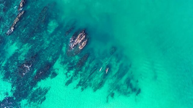 Drone aerial landscape of people in kayaks and outrigger canoes paddling over rocky reef inlet at sandy ocean beach bay channel near Tomakin Mossy Point South Coast Australia recreation and outdoors