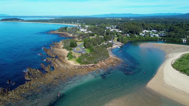 Drone aerial landscape of the flowing Tomaga River channel surrounded by rocky headland terrain coastline at Mossy Point town suburbs near Tomakin Beach on the South Coast Australia tourism and nature