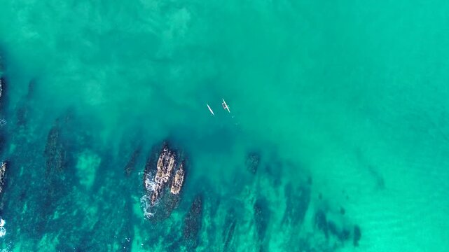 Drone aerial landscape of people engaging in ocean sports on the water surface near rocky island reef and sandbar along the coastline of Tomakin Beach South Coast NSW Australia leisure and recreation