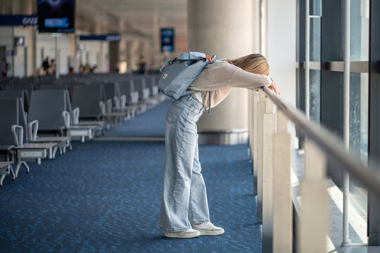 Frustrated woman traveler leaning on airport railing, exhausted after flight cancellation or missed departure. Travel stress, uncertainty during disrupted journey, delay, ruined plans, travel anxiety 