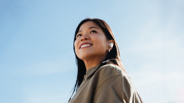Woman with earbuds smiling outdoors and looking up