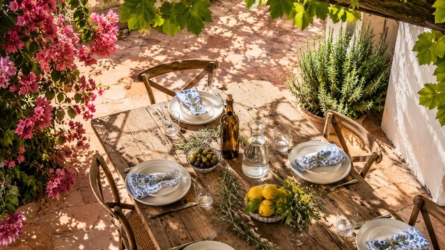 Rustic outdoor dining table setup in a beautiful Mediterranean garden under dappled summer sunlight