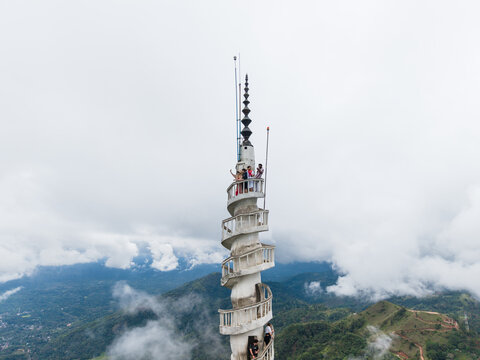 Gampola, Sri Lanka - 22 February 2026: Aerial view of Ambuluwawa Tower with its unique spiral staircase and tourists on the balcony overlooking misty green hills and clouds.
